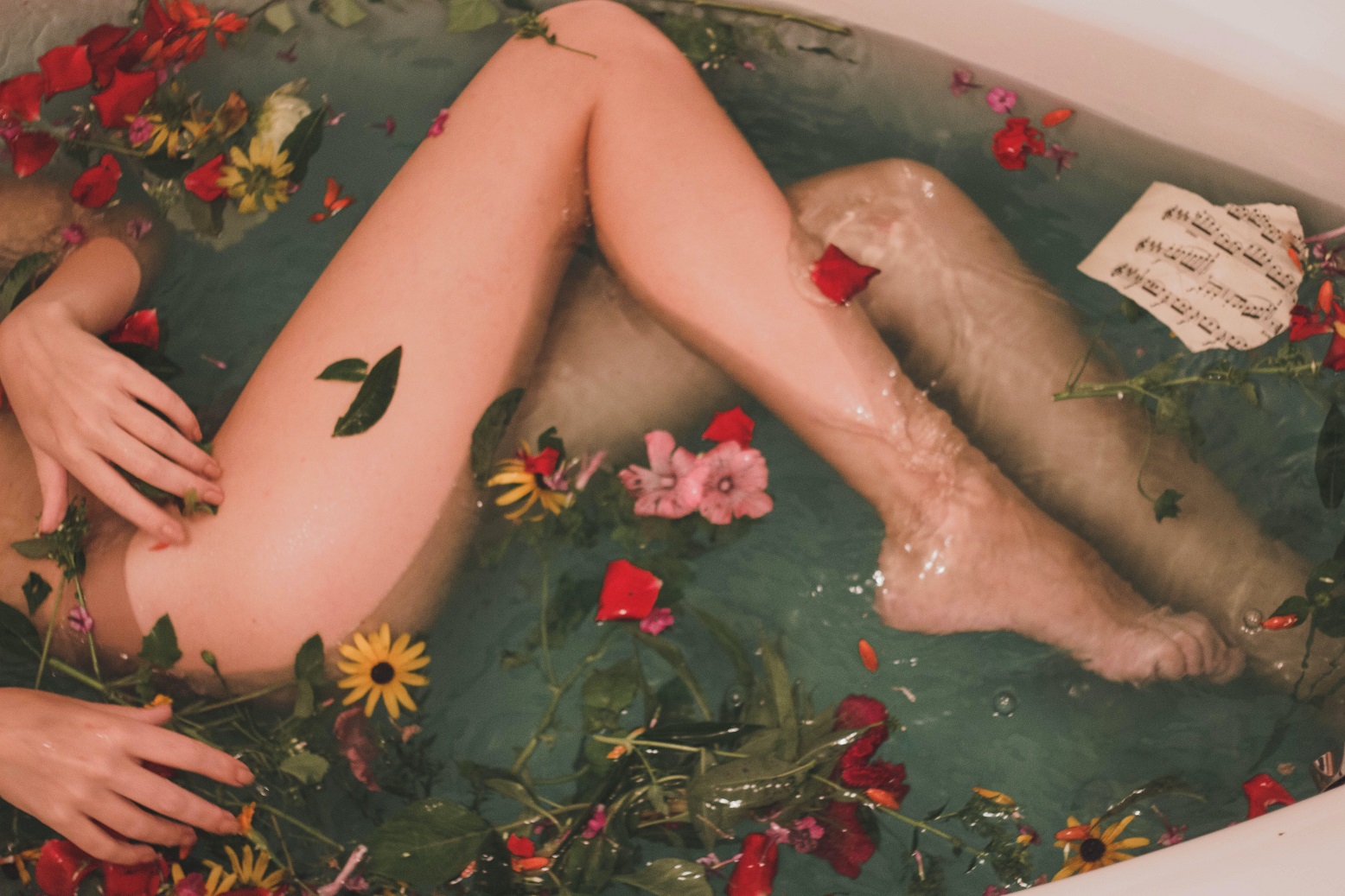 kobieta od pasa w dół kąpiąca się w wodzie pełnej płatków kwiatów