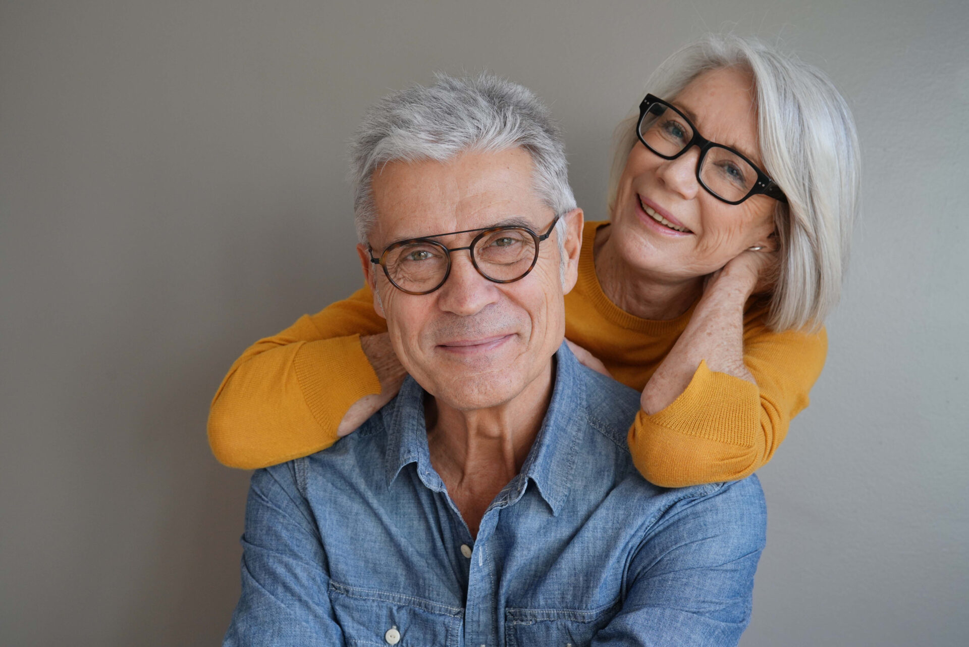 Portrait of relaxed fun senior couple wearing glasses on backgr