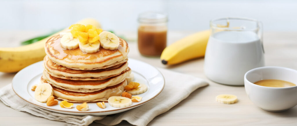 A stack of oatmeal banana pancakes with fresh banana slices, walnuts and honey on top and a cup of tea on a white wooden background. A healthy breakfast. Copy space